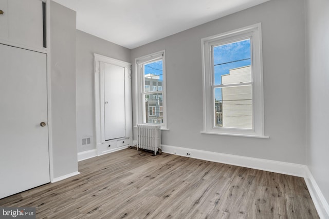 unfurnished bedroom featuring visible vents, radiator, baseboards, and wood finished floors