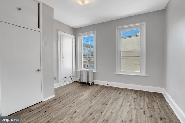 unfurnished bedroom with multiple windows, radiator, and wood finished floors