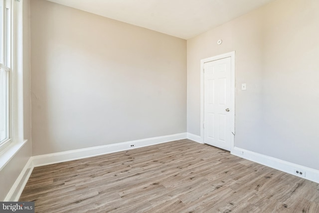 empty room featuring baseboards, a healthy amount of sunlight, and light wood finished floors