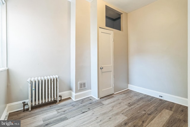 empty room with visible vents, radiator heating unit, baseboards, and wood finished floors