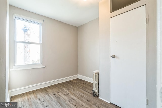 spare room with a wealth of natural light, baseboards, radiator, and wood finished floors