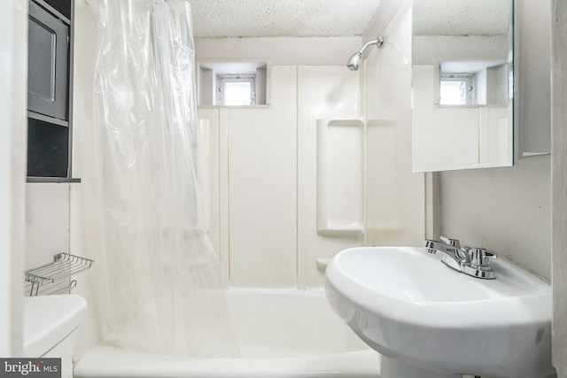 full bath featuring a sink, a textured ceiling, shower / tub combo, and toilet