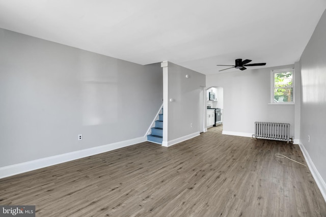 unfurnished living room featuring baseboards, stairway, radiator heating unit, wood finished floors, and arched walkways