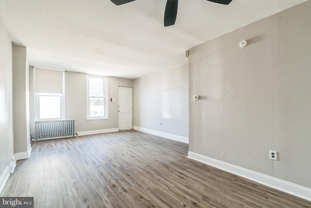 empty room with radiator, wood finished floors, and baseboards