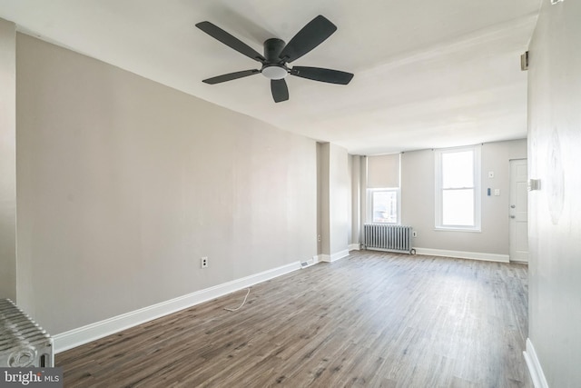 unfurnished living room with radiator, baseboards, and wood finished floors