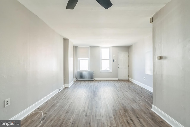 unfurnished living room with radiator, wood finished floors, baseboards, and ceiling fan