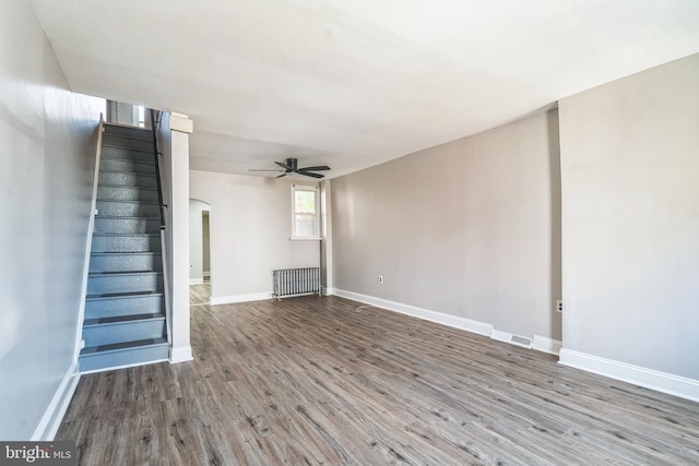 unfurnished living room featuring stairway, radiator, a ceiling fan, wood finished floors, and arched walkways