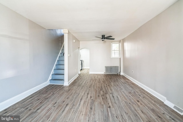 unfurnished living room with baseboards, stairway, radiator heating unit, wood finished floors, and arched walkways