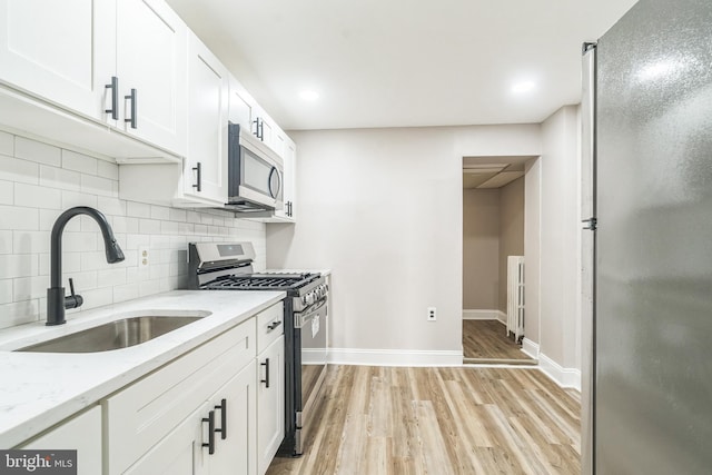 kitchen with a sink, stainless steel appliances, white cabinetry, light wood-type flooring, and backsplash