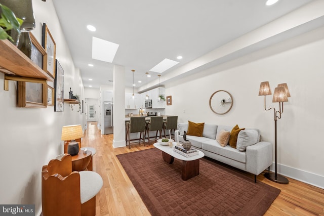 living room with baseboards, recessed lighting, a skylight, and light wood-style floors