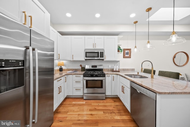 kitchen with a sink, stainless steel appliances, a peninsula, white cabinets, and light wood finished floors