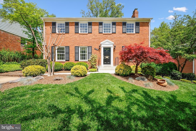 colonial inspired home featuring a chimney, brick siding, and a front yard
