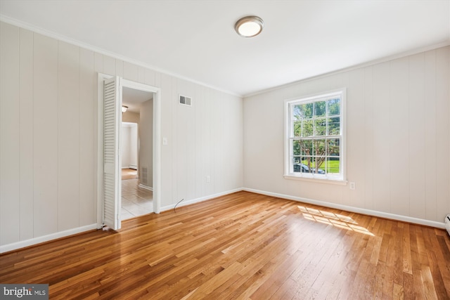 empty room with crown molding, baseboards, hardwood / wood-style floors, and visible vents