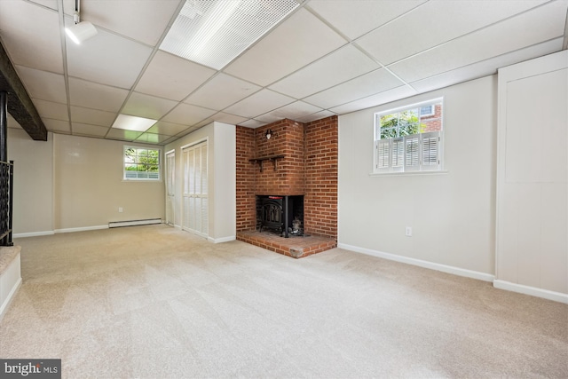 unfurnished living room with carpet floors, a wood stove, a drop ceiling, and baseboard heating