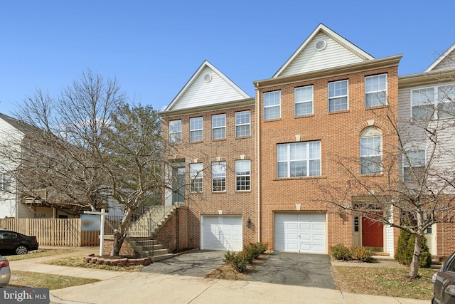 multi unit property with fence, driveway, stairs, a garage, and brick siding