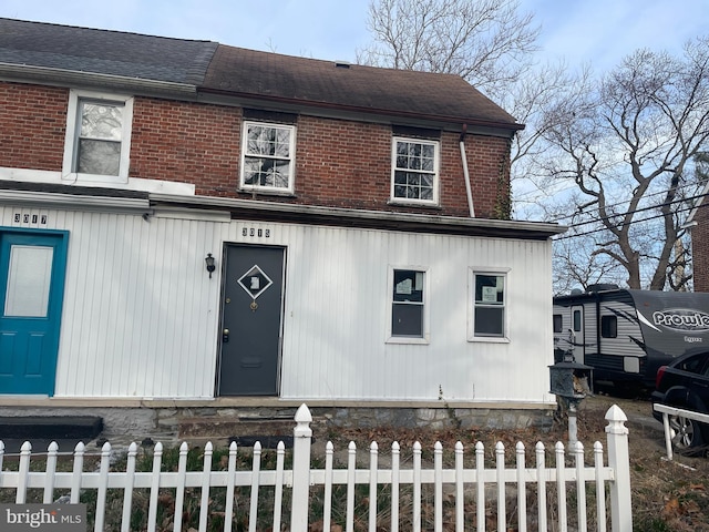 view of property featuring brick siding, a fenced front yard, and roof with shingles