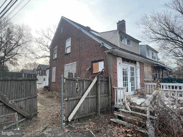 view of property exterior with brick siding, french doors, a chimney, and fence