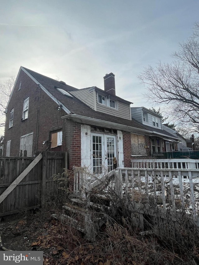 rear view of property featuring brick siding, a chimney, and fence