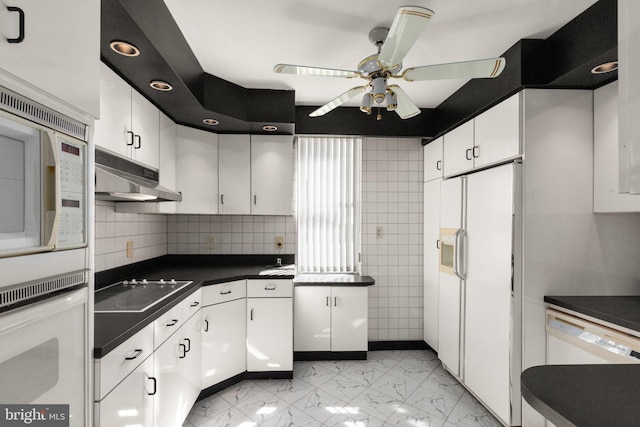 kitchen featuring a ceiling fan, under cabinet range hood, dark countertops, white appliances, and white cabinets