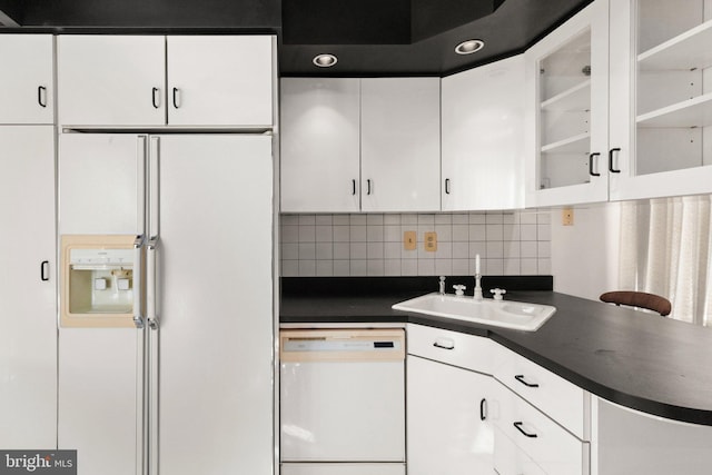 kitchen with dark countertops, white appliances, white cabinetry, and a sink