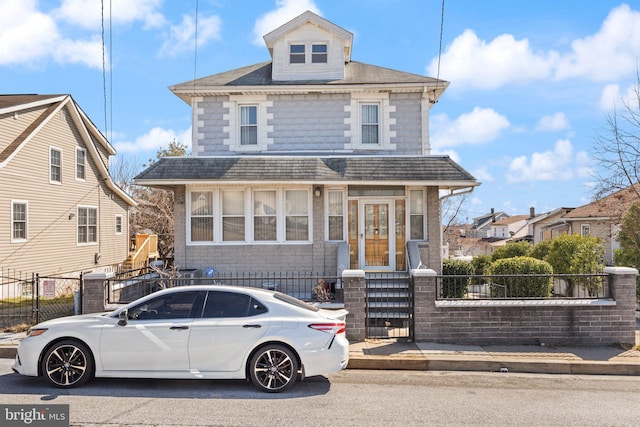 american foursquare style home with a fenced front yard and a shingled roof