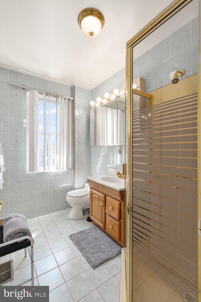 bathroom featuring tile patterned floors, toilet, a stall shower, tile walls, and vanity