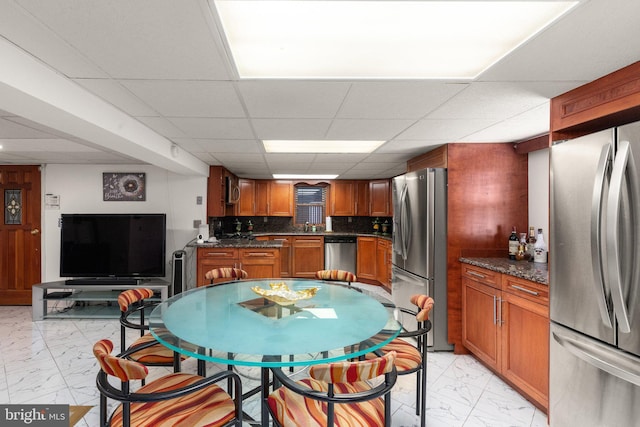 kitchen with stainless steel appliances, decorative backsplash, a paneled ceiling, marble finish floor, and brown cabinets