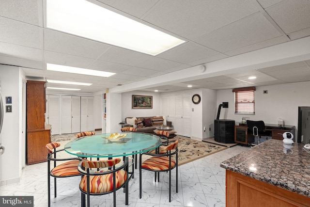 dining room with marble finish floor, a wood stove, baseboards, and a paneled ceiling