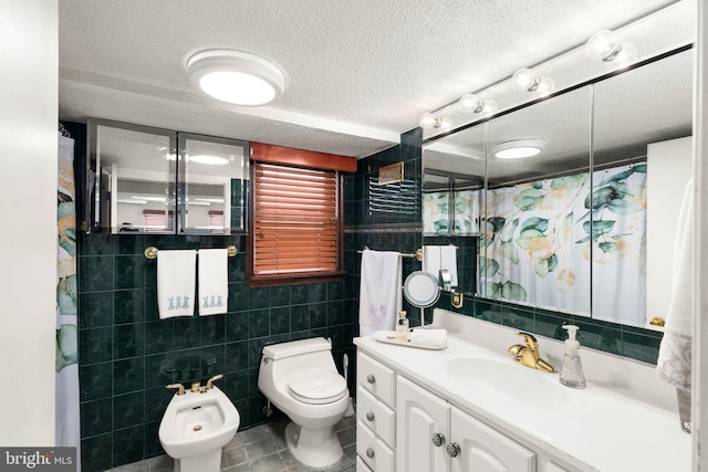 bathroom with toilet, vanity, a bidet, a textured ceiling, and tile walls