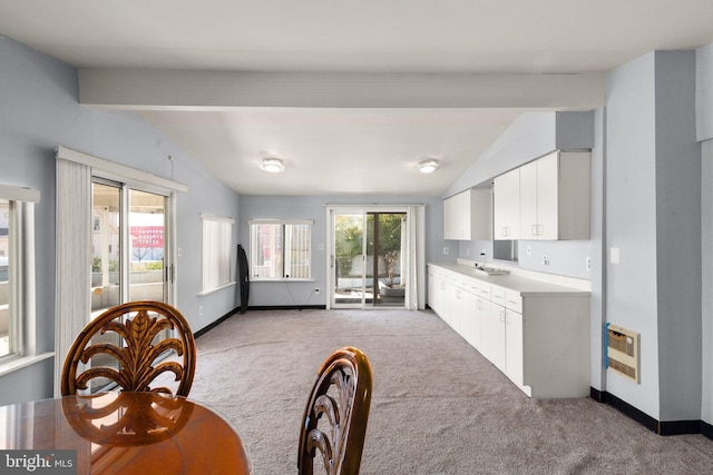 carpeted dining room featuring heating unit, vaulted ceiling with beams, a wealth of natural light, and a sink