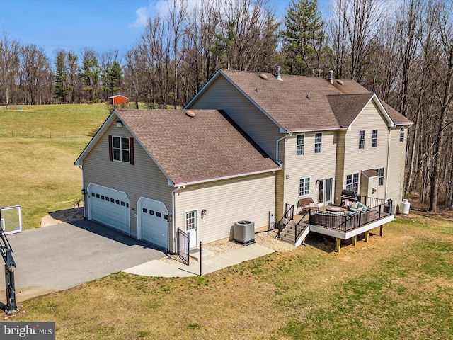 back of property with a deck, cooling unit, roof with shingles, a lawn, and driveway