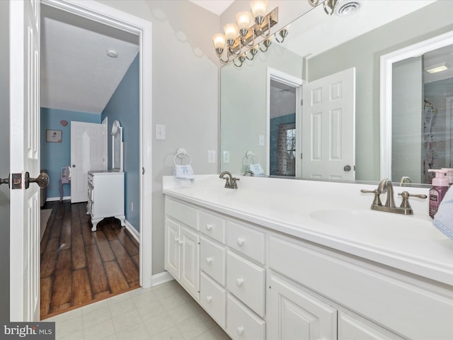 full bath with baseboards, double vanity, a sink, and a notable chandelier
