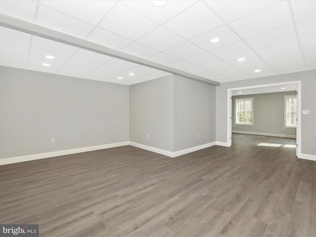 below grade area featuring baseboards, a paneled ceiling, and dark wood finished floors