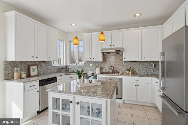 kitchen with under cabinet range hood, backsplash, appliances with stainless steel finishes, white cabinets, and light tile patterned floors