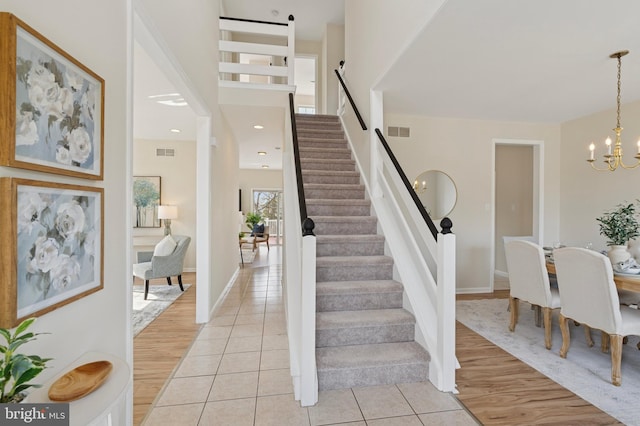 staircase featuring tile patterned floors, visible vents, baseboards, and a chandelier