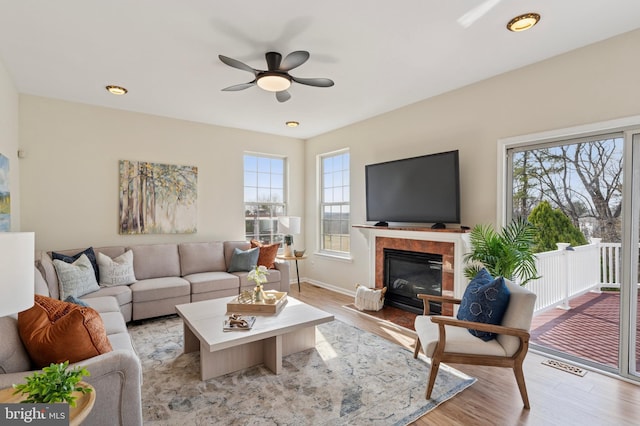 living room featuring a glass covered fireplace, light wood finished floors, visible vents, and a wealth of natural light