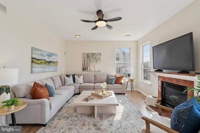 living room featuring light wood-type flooring, visible vents, a ceiling fan, a premium fireplace, and baseboards