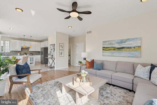 living room with a ceiling fan, visible vents, baseboards, recessed lighting, and light wood-style floors