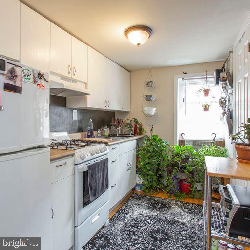 kitchen featuring under cabinet range hood, decorative backsplash, white appliances, and white cabinets