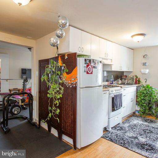 kitchen featuring white appliances, extractor fan, white cabinets, light countertops, and light wood-style floors