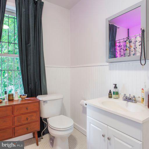 bathroom with a wainscoted wall, toilet, vanity, and tile patterned flooring