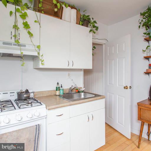 kitchen with white cabinets, white range with gas stovetop, under cabinet range hood, and a sink