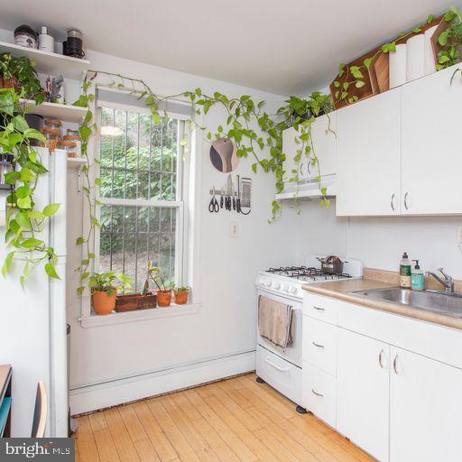 kitchen featuring light wood finished floors, gas range gas stove, light countertops, white cabinetry, and a sink