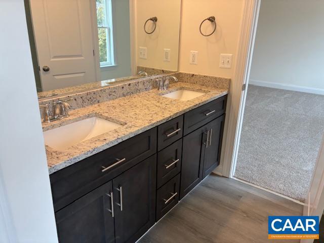 full bathroom featuring double vanity, wood finished floors, baseboards, and a sink