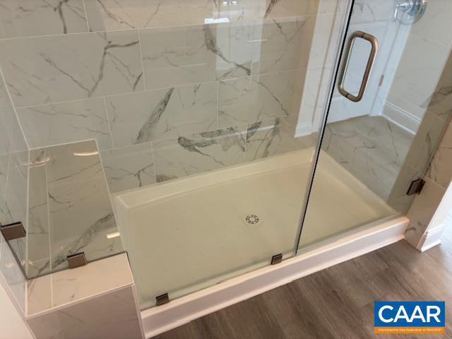 full bathroom with a marble finish shower and wood finished floors