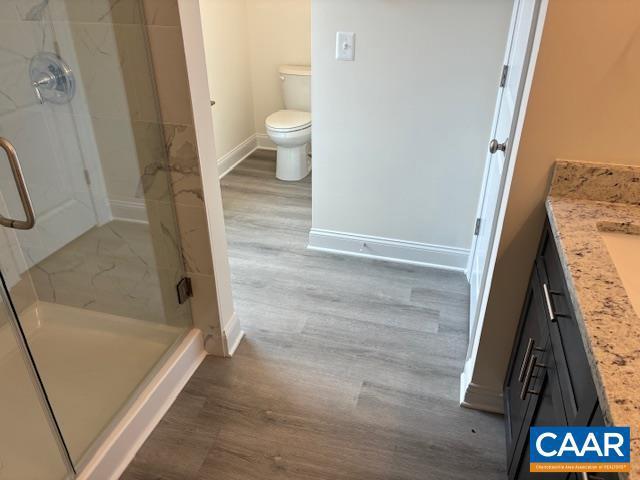 bathroom with a shower stall, toilet, baseboards, and wood finished floors