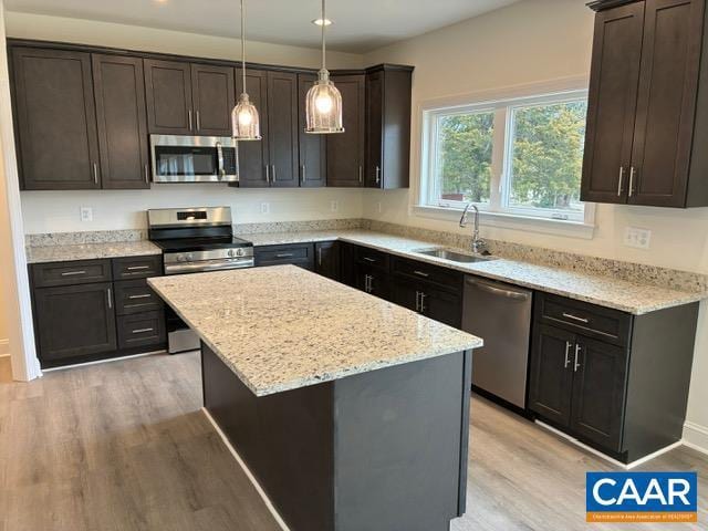 kitchen with light stone counters, a kitchen island, a sink, appliances with stainless steel finishes, and light wood-type flooring