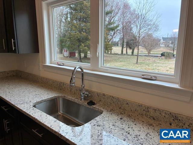 kitchen featuring dark cabinets, a healthy amount of sunlight, light stone countertops, and a sink