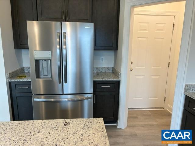 kitchen with wood finished floors, light stone counters, and stainless steel fridge with ice dispenser