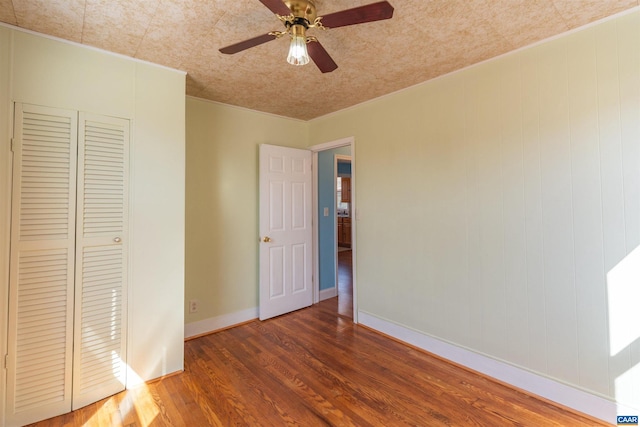 unfurnished bedroom featuring a ceiling fan, wood finished floors, baseboards, and a closet